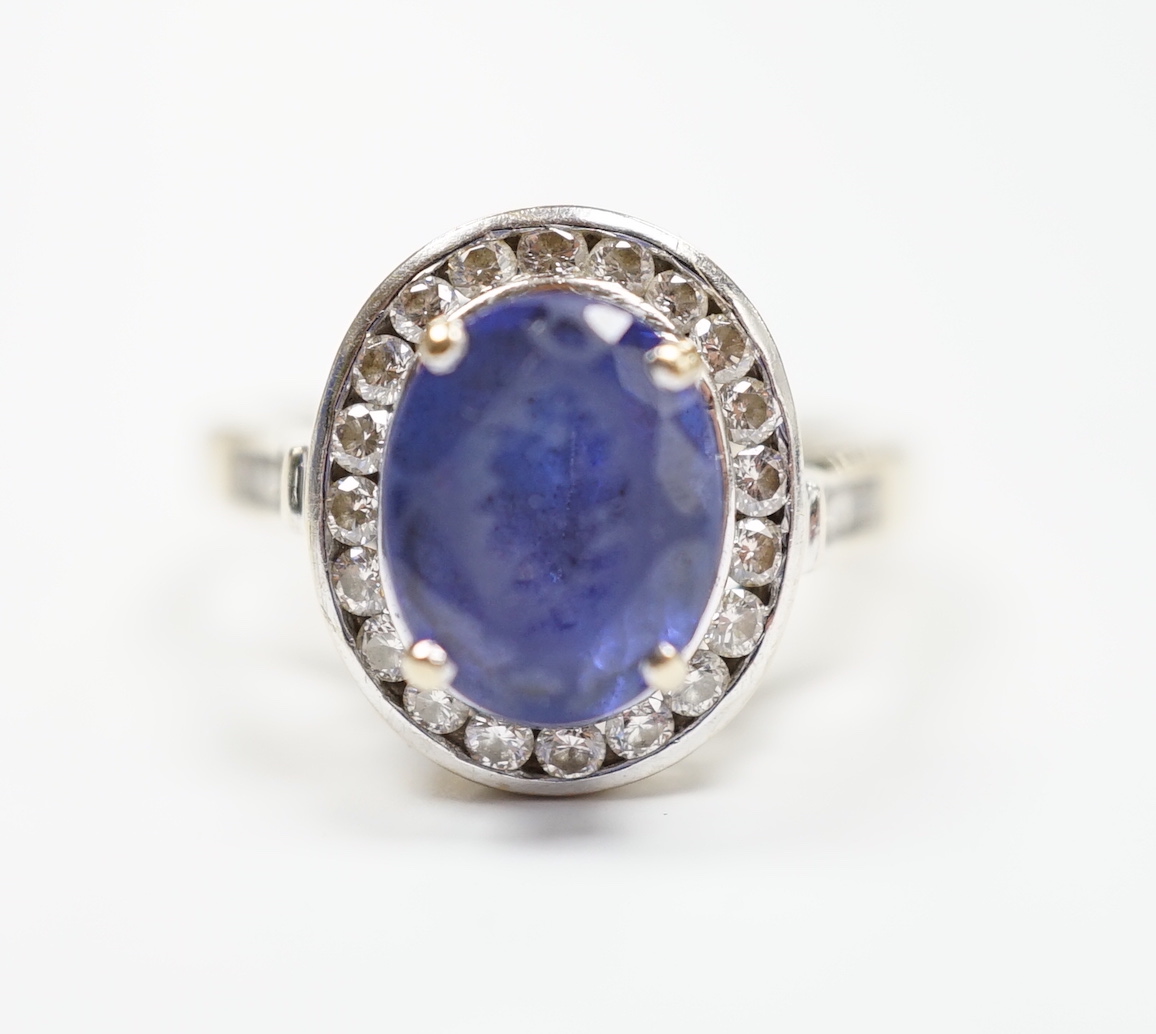 A modern 750 and oval cut single stone tanzanite(worn) set dress ring, with diamond set border and shoulders, size P, gross weight 8.9 grams.